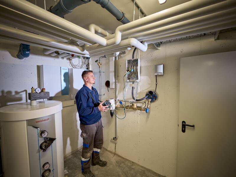 Ein Mann steht in einem Technikraum mit Rohren und einer Heizungsanlage.