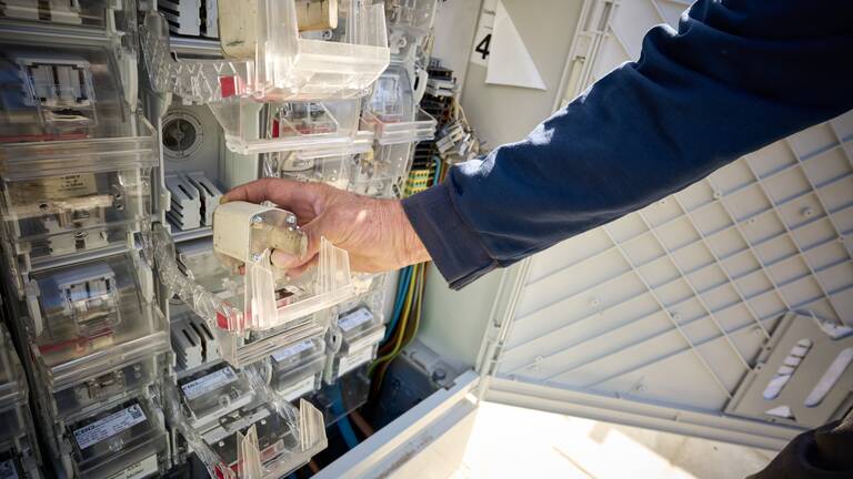 Eine Person in einem blauen Pullover arbeitet an einer elektrischen Schalttafel und hält eine Schutzabdeckung in der Hand.