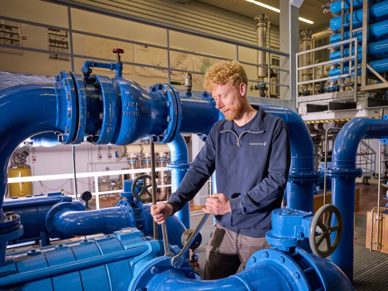 Wassermonteur erledigt Wartungsarbeiten in einem Hochbehälter mit vielen blauen Wasserrohren