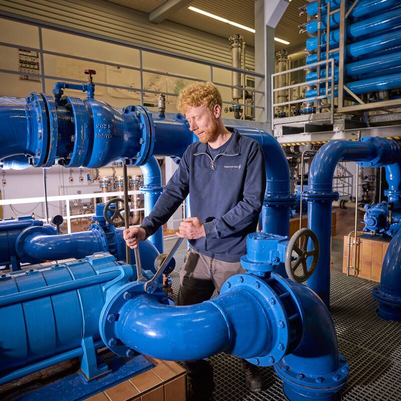 Wassermonteur erledigt Wartungsarbeiten in einem Hochbehälter mit vielen blauen Wasserrohren