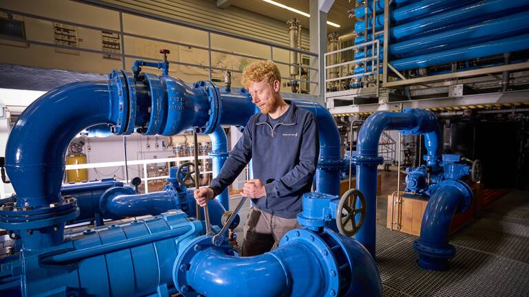 Wassermonteur erledigt Wartungsarbeiten in einem Hochbehälter mit vielen blauen Wasserrohren