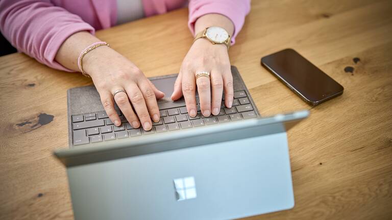 Das Foto zeigt eine Frau die Daten an einem Laptop eingiebt mit einer rosa Weste an