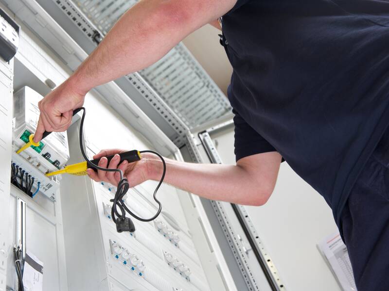Eine Person arbeitet an einem elektrischen Schaltschrank und benutzt ein Prüfgerät.