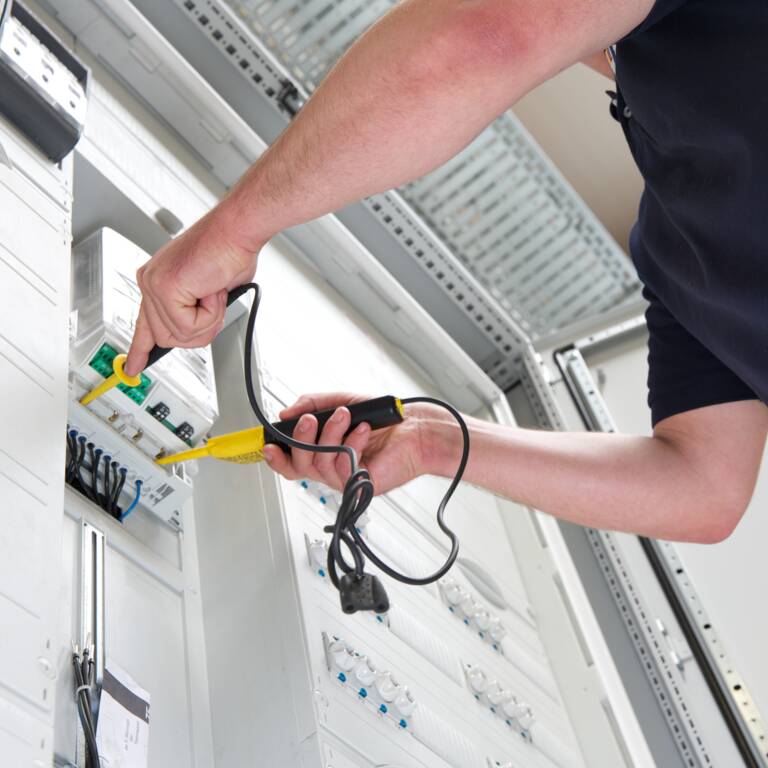 Eine Person arbeitet an einem elektrischen Schaltschrank und benutzt ein Prüfgerät.