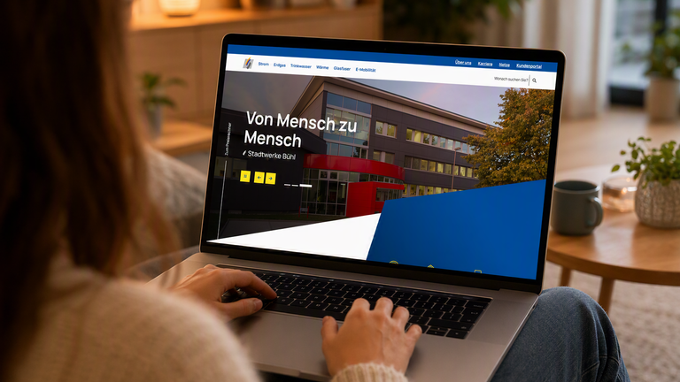 Eine Person sitzt vor einem Laptop, der eine Webseite der Stadtwerke Bühl mit dem Slogan "Von Mensch zu Mensch" anzeigt.